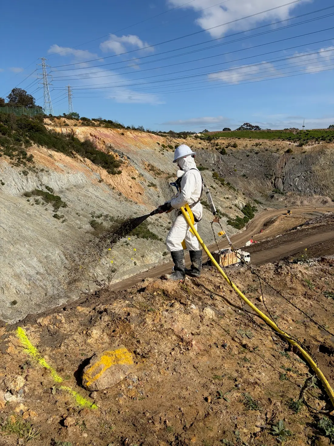 Harnessed Core Environmental Projects operator spraying Posi-Shell down a steep landfill batter from the crest